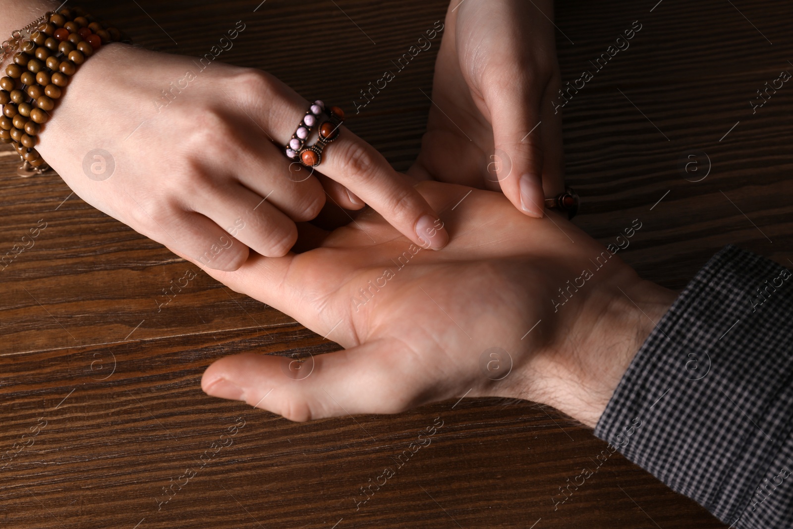 Photo of Chiromancer reading lines on man's palm at table, closeup