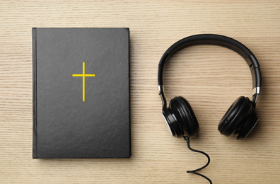 Photo of Bible and headphones on wooden background, top view. Religious audiobook