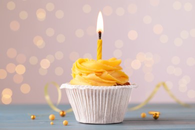 Photo of Tasty birthday cupcake on light blue wooden table against blurred lights