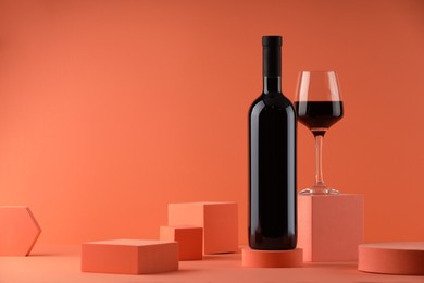 Stylish presentation of delicious red wine in bottle and glass on orange background. Space for text