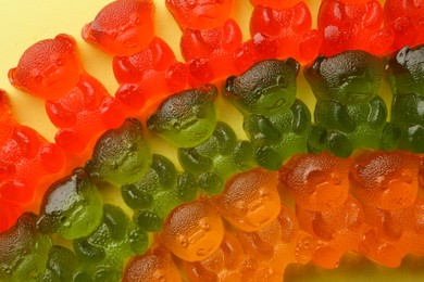 Photo of Different delicious gummy bear candies on yellow background, flat lay