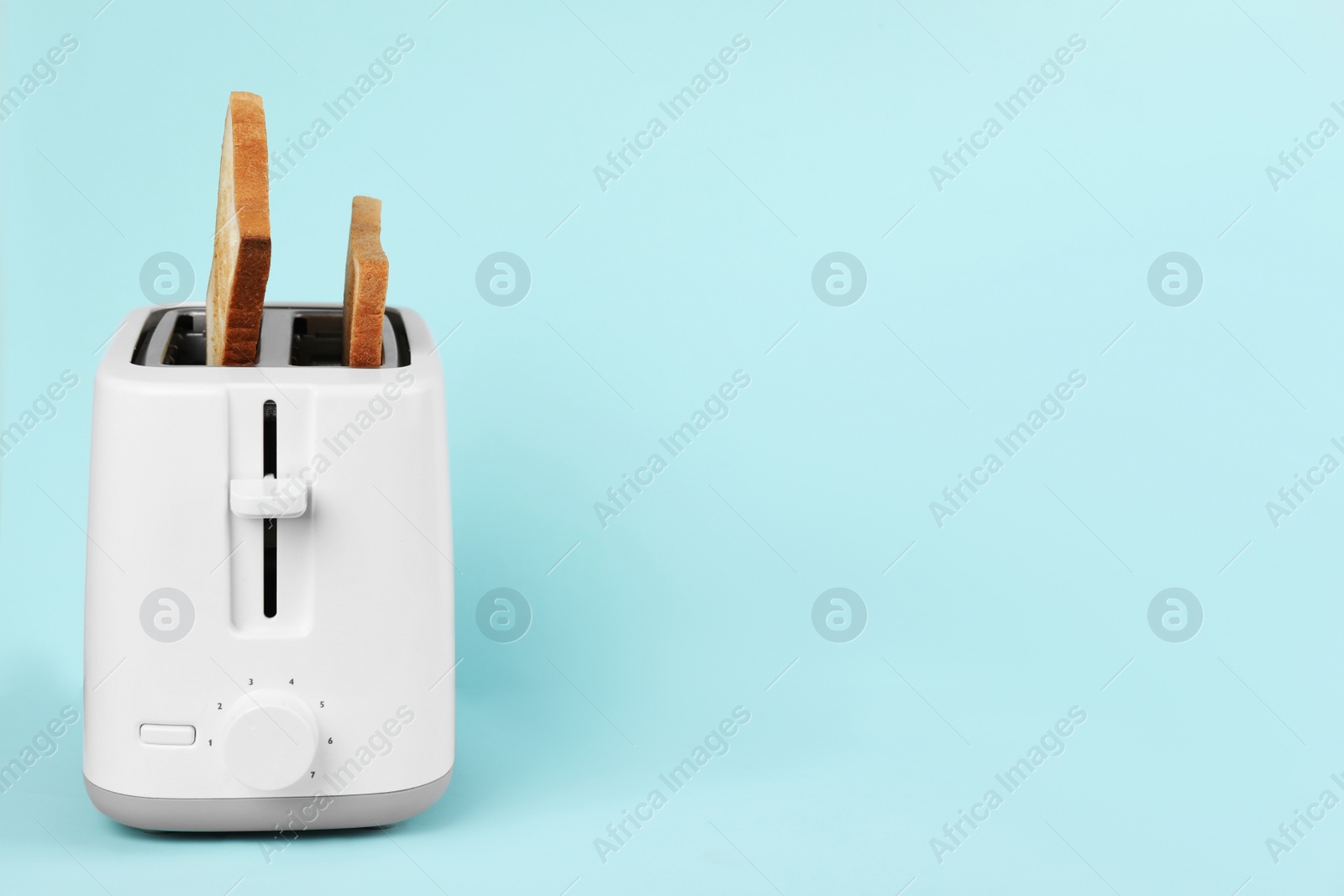 Photo of Modern toaster with slices of bread on light blue background. Space for text