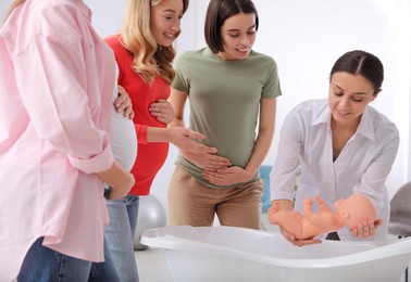 Photo of Pregnant women learning how to bathe baby at courses for expectant mothers indoors