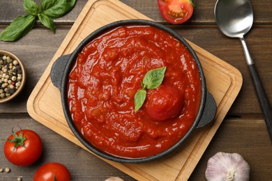 Photo of Homemade tomato sauce in bowl, spoon and ingredients on wooden table, flat lay