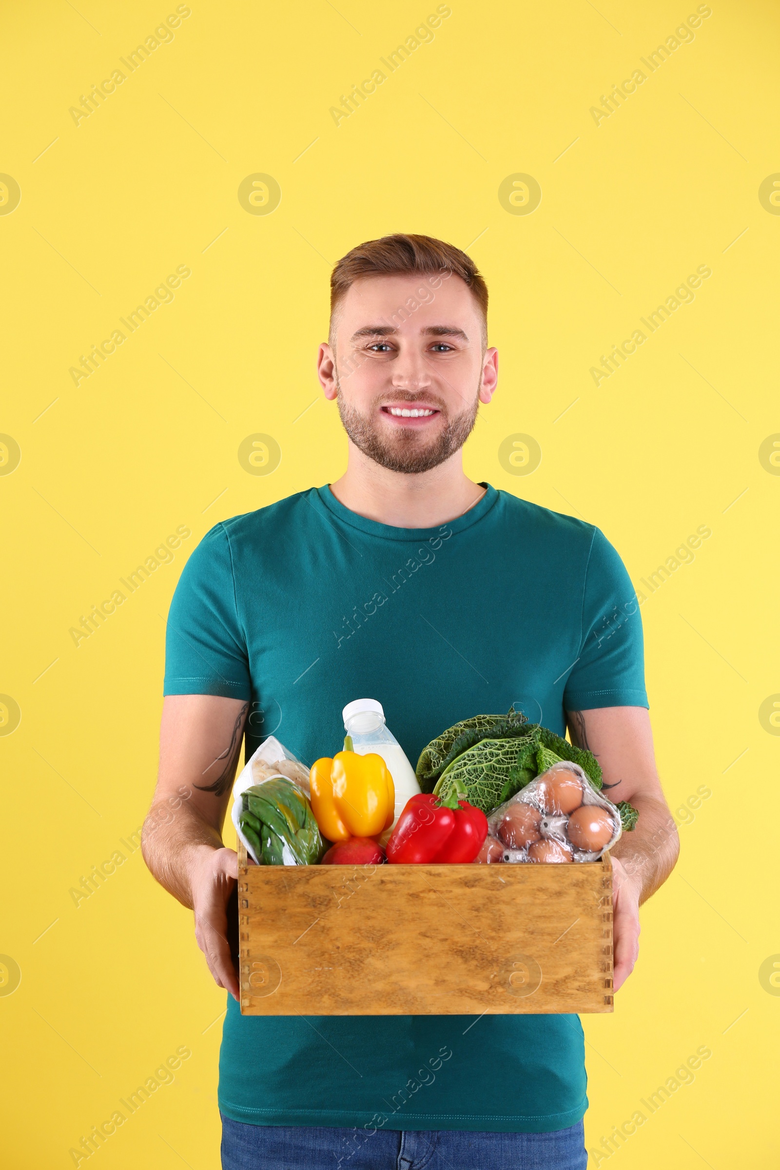 Photo of Delivery man holding wooden crate with food products on color background