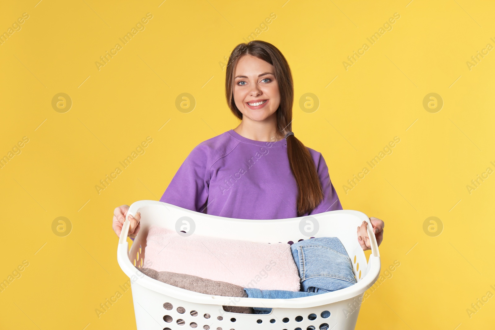 Photo of Happy young woman holding basket with laundry on color background