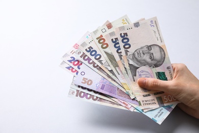 Photo of Woman holding Ukrainian money on light grey background, closeup
