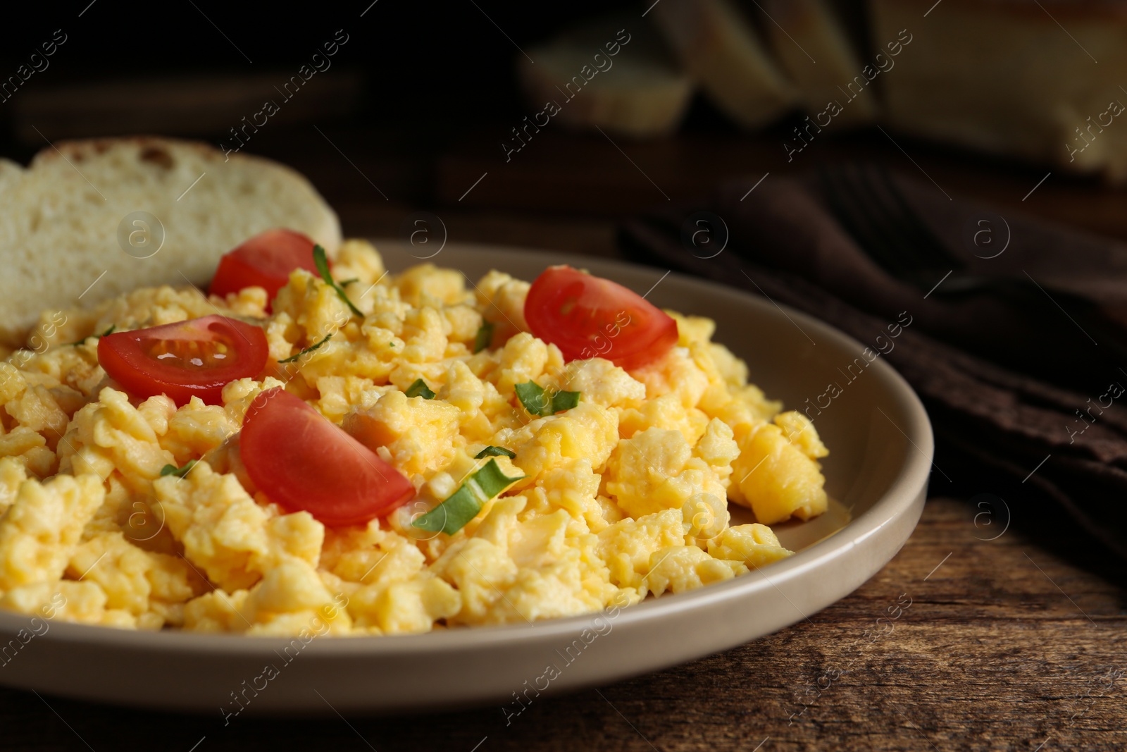 Photo of Tasty scrambled eggs with cherry tomato and bread on wooden table, closeup