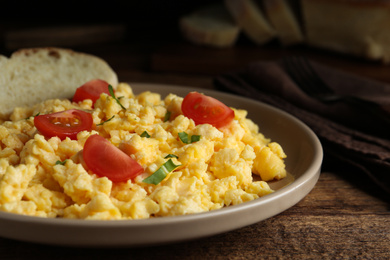 Photo of Tasty scrambled eggs with cherry tomato and bread on wooden table, closeup