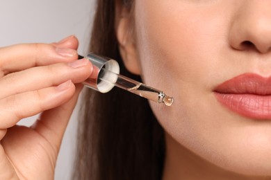 Young woman applying essential oil onto face on light grey background, closeup