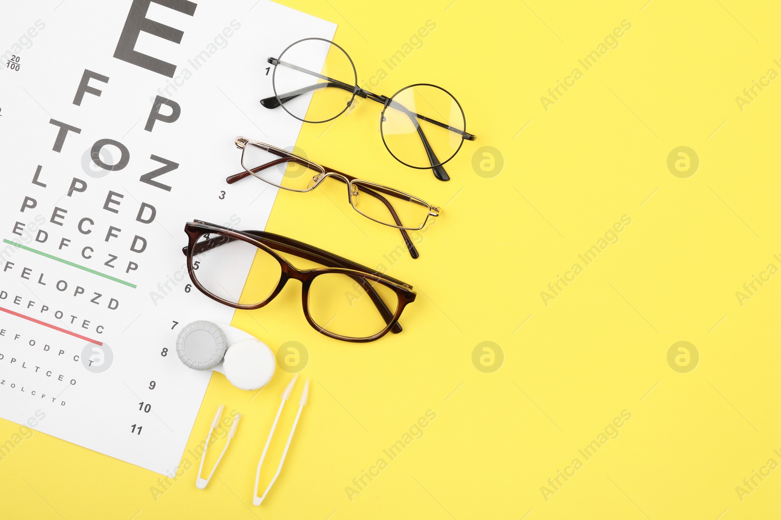 Photo of Vision test chart, glasses, lenses and tweezers on yellow background, flat lay. Space for text