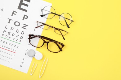 Photo of Vision test chart, glasses, lenses and tweezers on yellow background, flat lay. Space for text