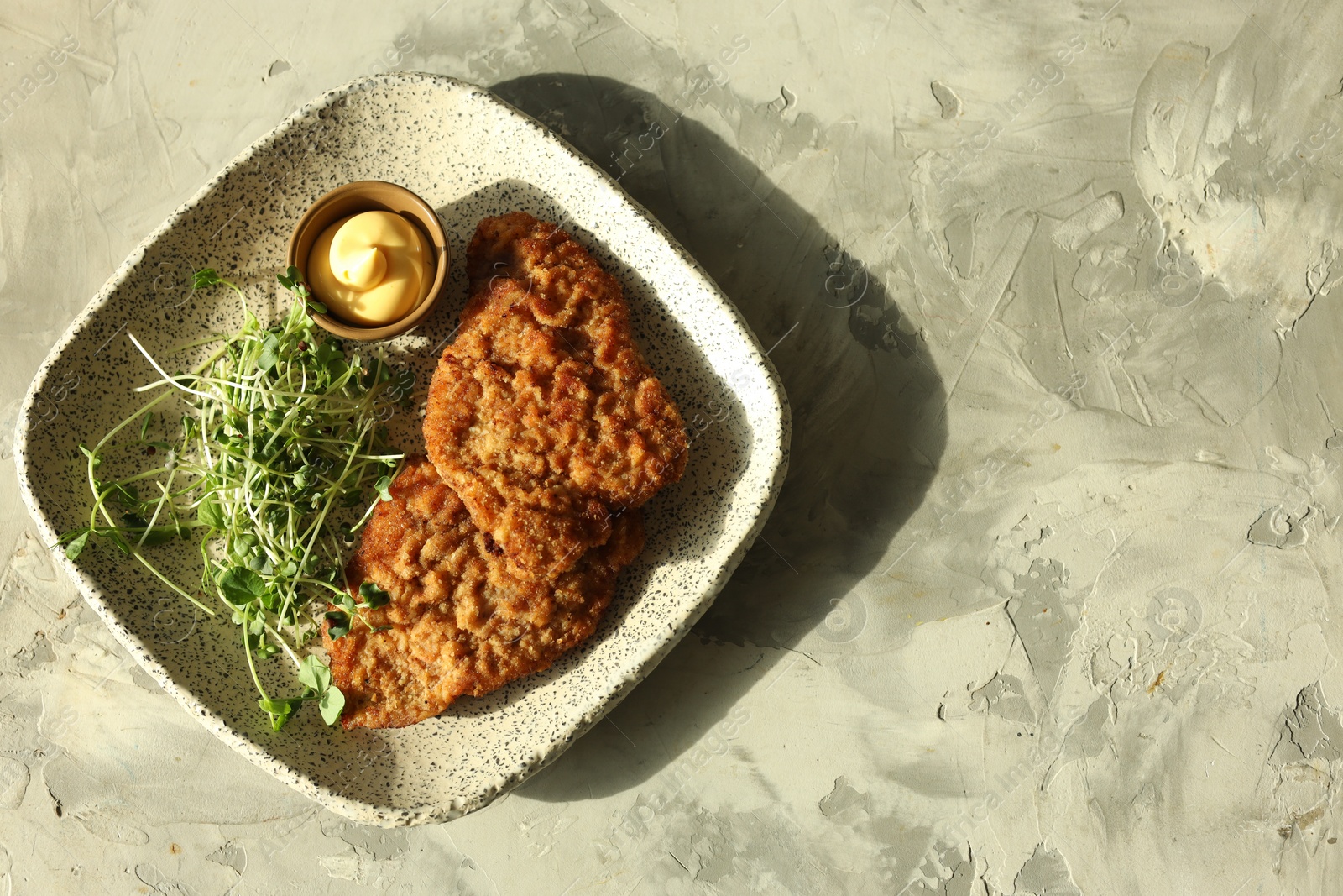 Photo of Tasty schnitzels served with sauce and microgreens on grey textured table, top view. Space for text