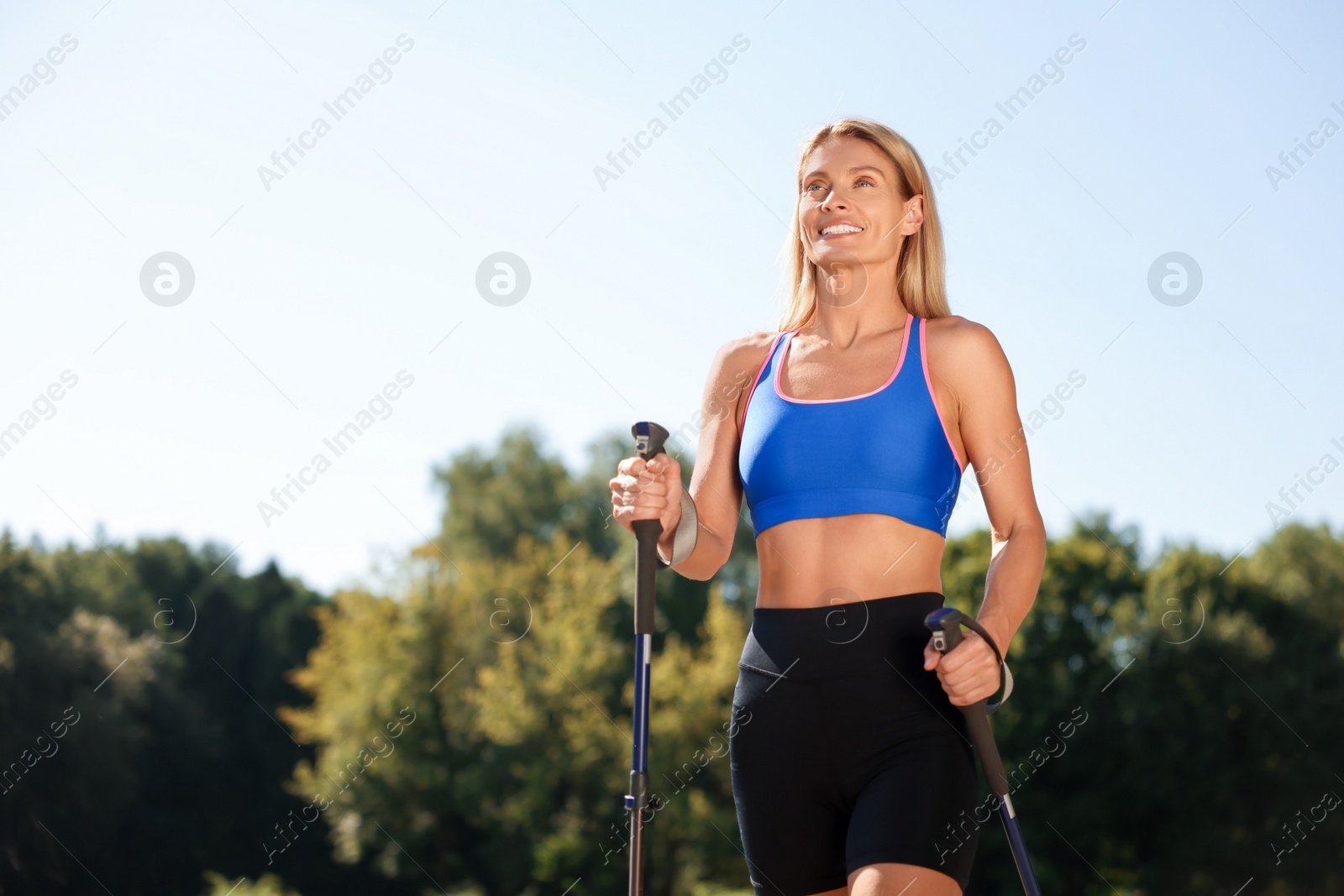 Photo of Happy woman practicing Nordic walking with poles outdoors on sunny day