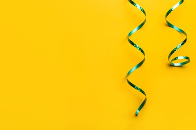 Shiny green serpentine streamers on yellow background, flat lay. Space for text
