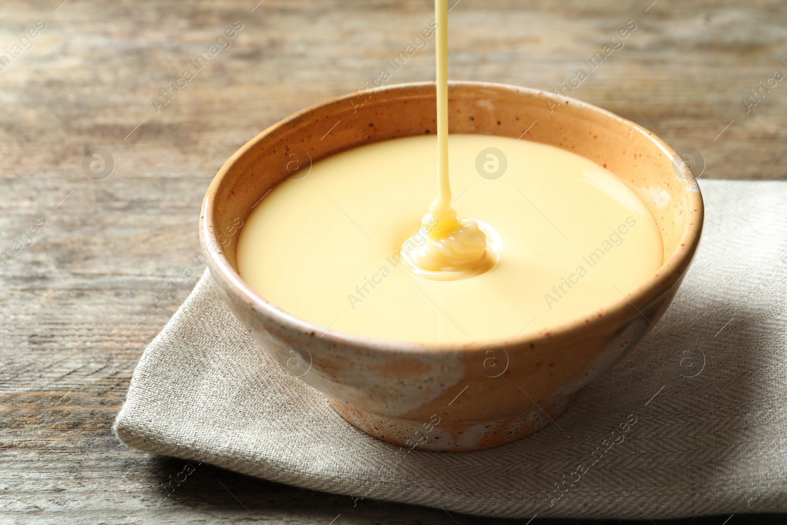 Photo of Condensed milk pouring into bowl on table, closeup