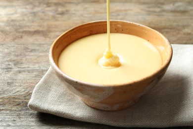 Condensed milk pouring into bowl on table, closeup