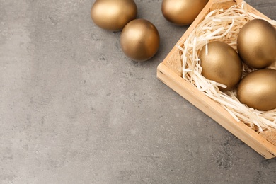 Wooden crate with golden eggs on color background, top view. Space for text