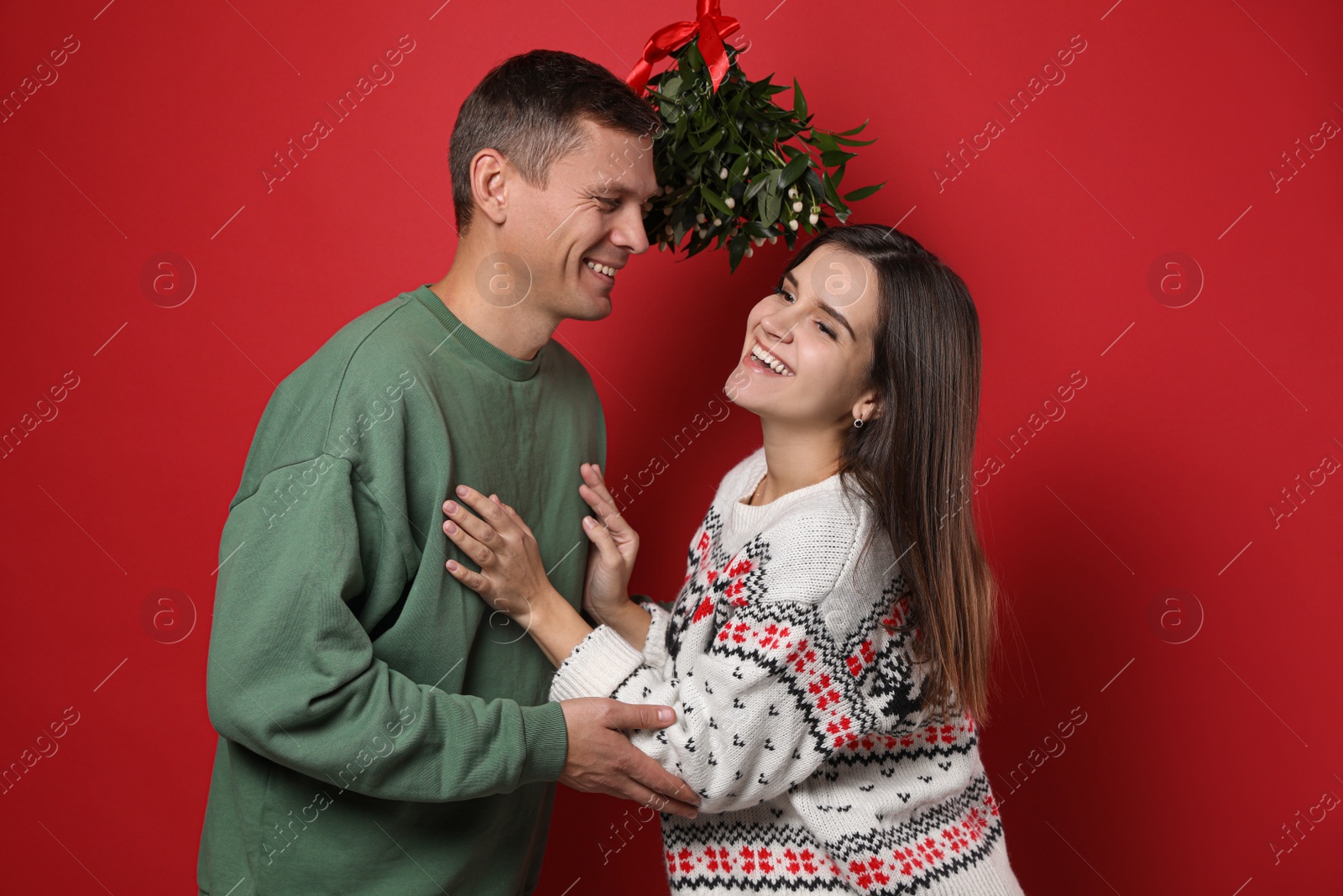 Photo of Happy couple standing under mistletoe bunch on red background
