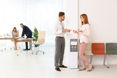 Photo of Co-workers having break near water cooler at workplace. Space for text