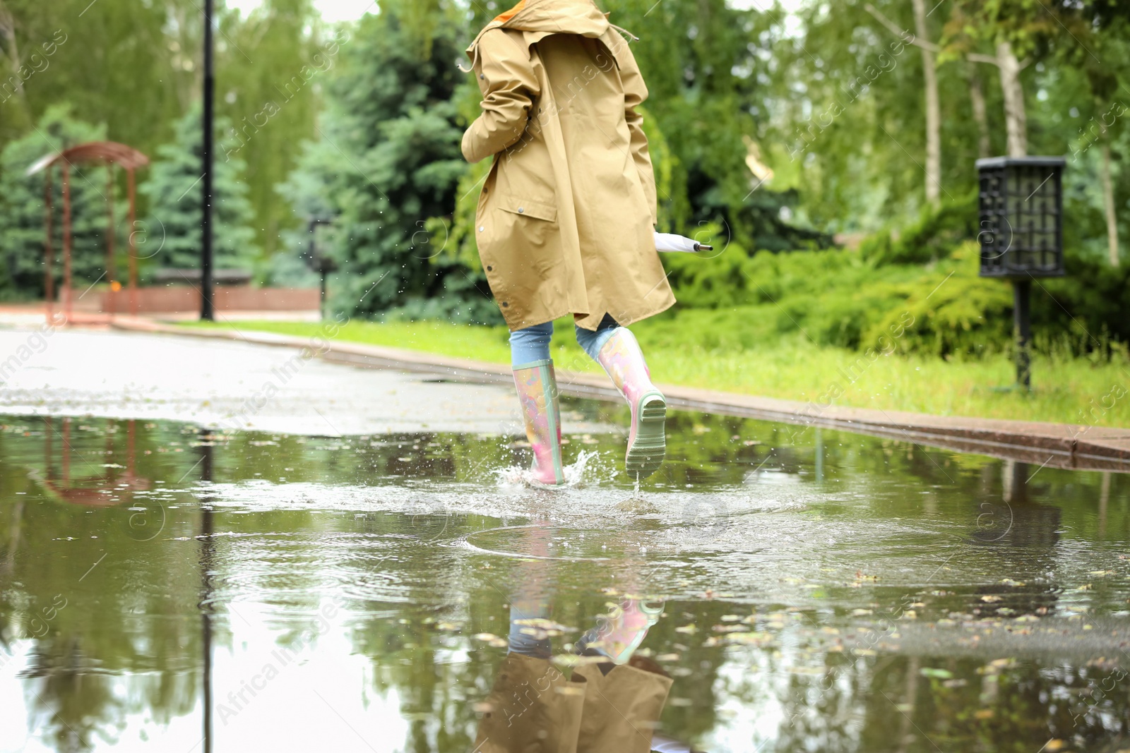 Photo of Woman with rubber boots running in puddle, closeup. Rainy weather