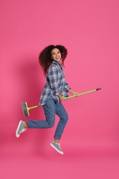 Photo of African American woman with green broom jumping on pink background