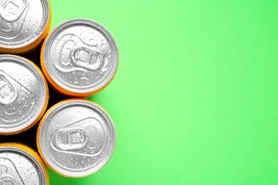 Photo of Energy drinks in wet cans on green background, top view. Space for text