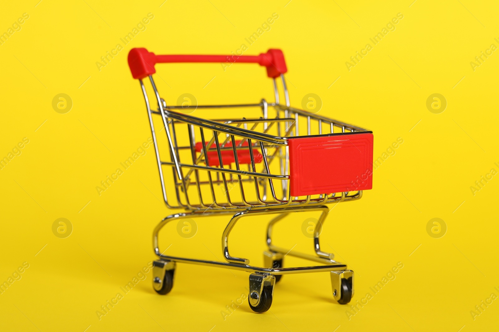 Photo of Small metal shopping cart on yellow background