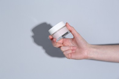 Woman holding jar of cream on grey background, closeup. Space for text