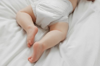 Photo of Little baby in diaper on white bed, closeup