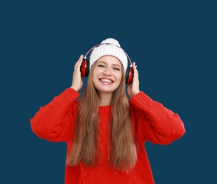 Young woman listening to music with headphones on dark blue background