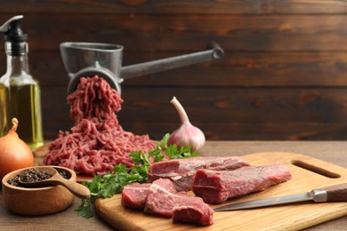 Photo of Manual meat grinder with beef, garlic, onion, parsley, oil and peppercorns on wooden table, space for text