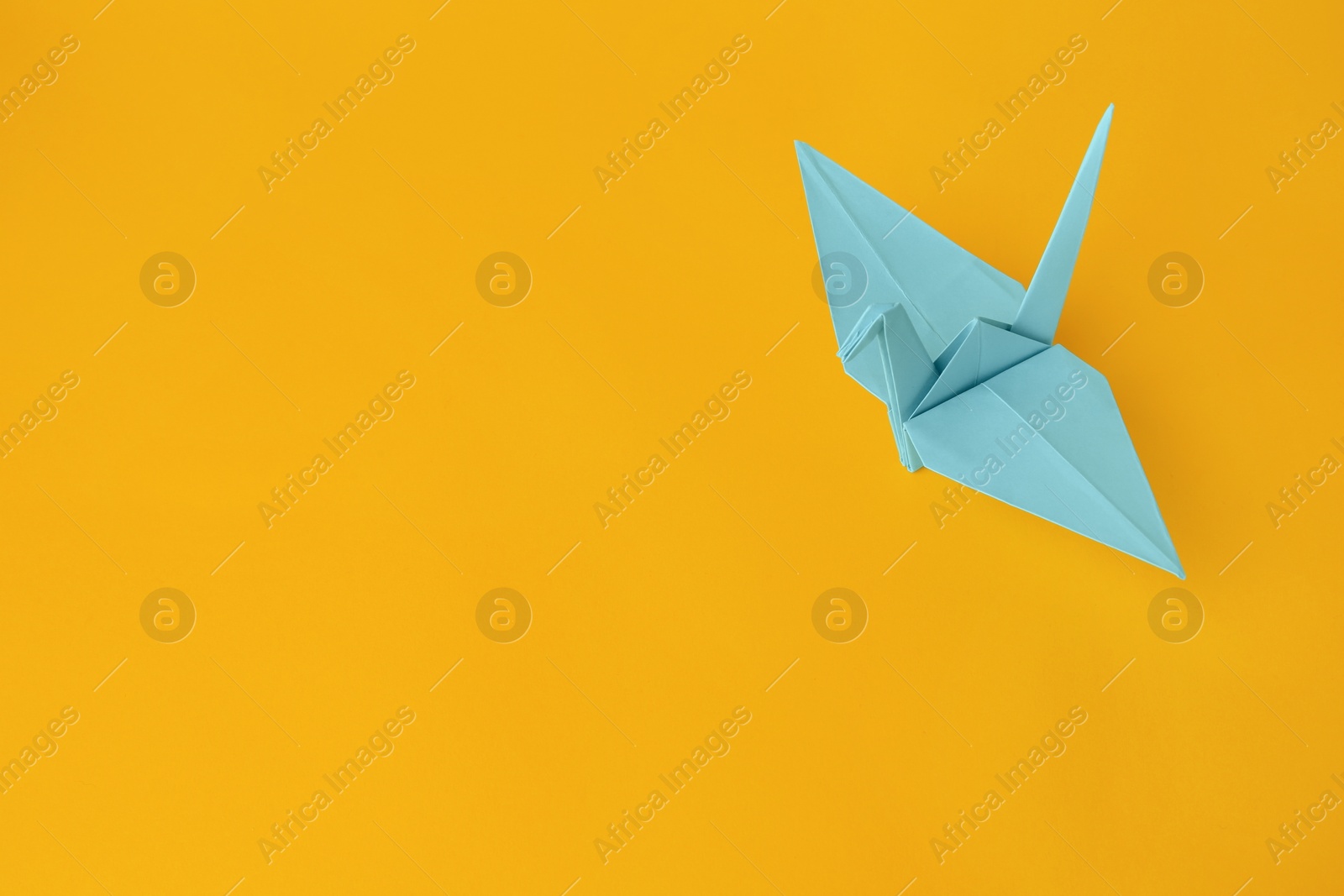 Photo of Origami art. Beautiful light blue paper crane on orange background, space for text