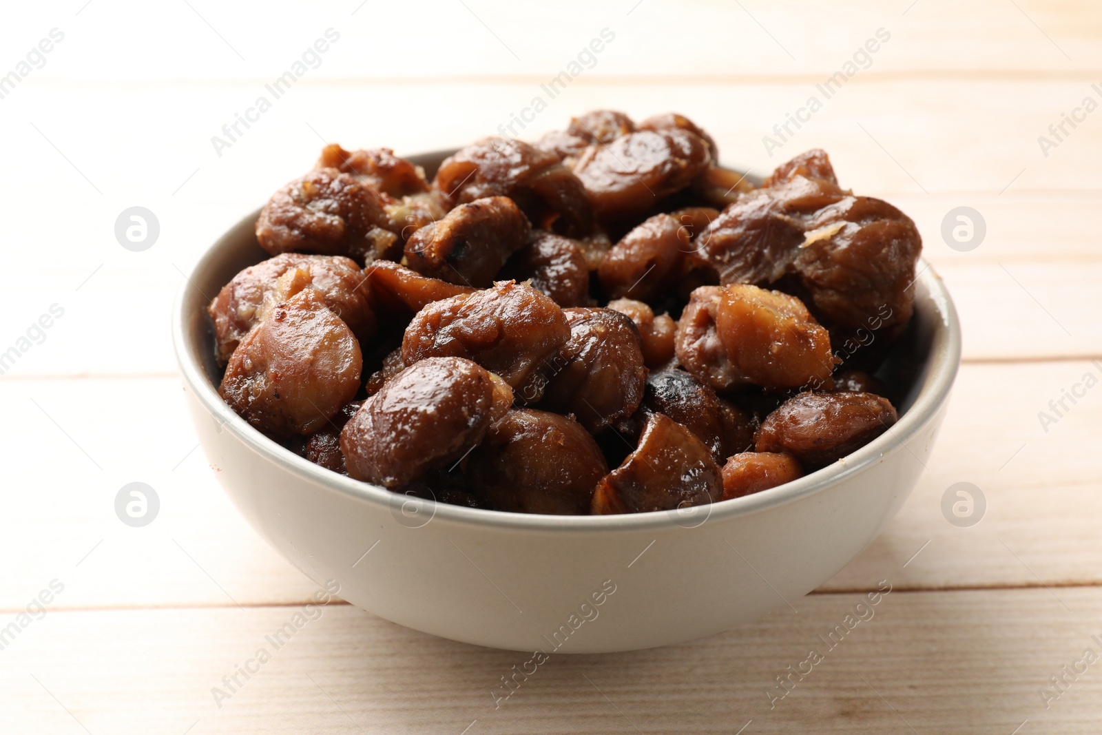 Photo of Roasted edible sweet chestnuts in bowl on light wooden table, closeup