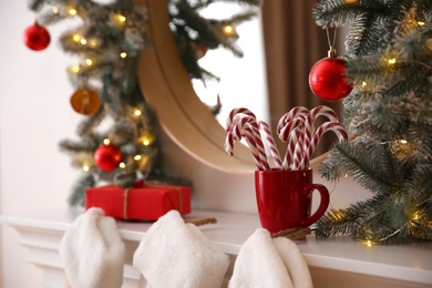 Photo of Candy canes in cup near mirror with Christmas garland, closeup