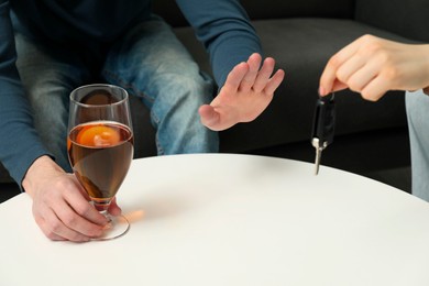 Photo of Man with glass of alcoholic drink refusing drive car while woman suggesting him keys, closeup. Don't drink and drive concept