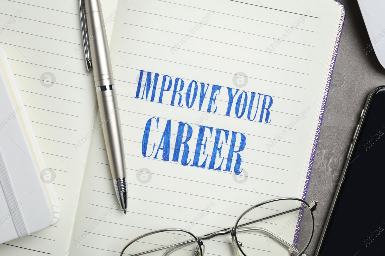 Photo of Notebook with words IMPROVE YOUR CAREER, pen and glasses on table, closeup