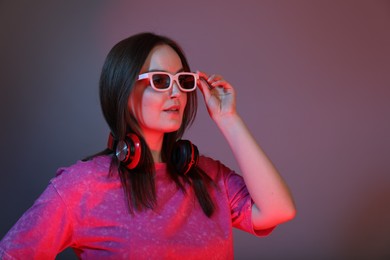 Stylish woman with headphones wearing sunglasses on color background, space for text