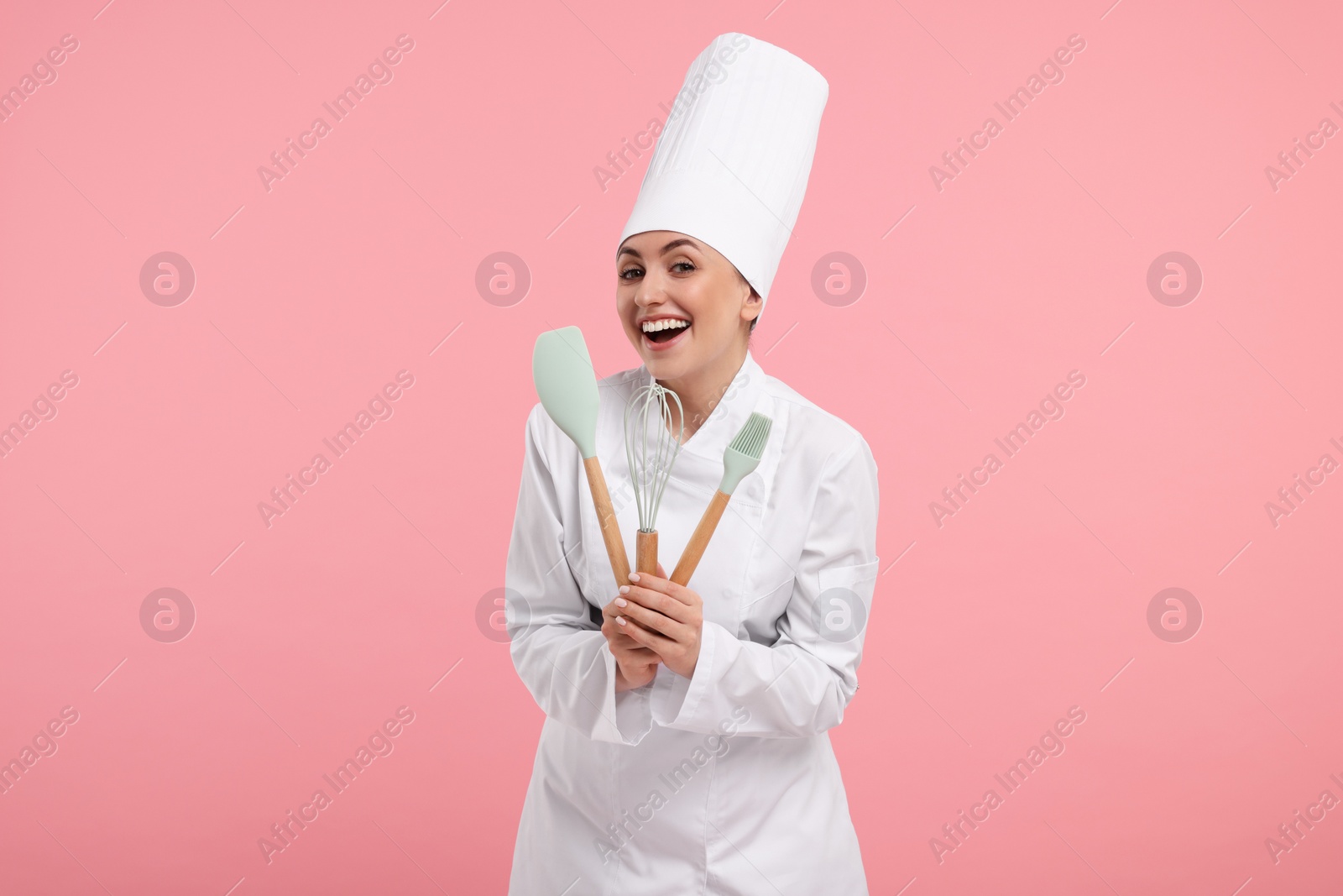 Photo of Happy confectioner in uniform holding professional tools on pink background