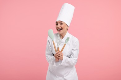 Photo of Happy confectioner in uniform holding professional tools on pink background