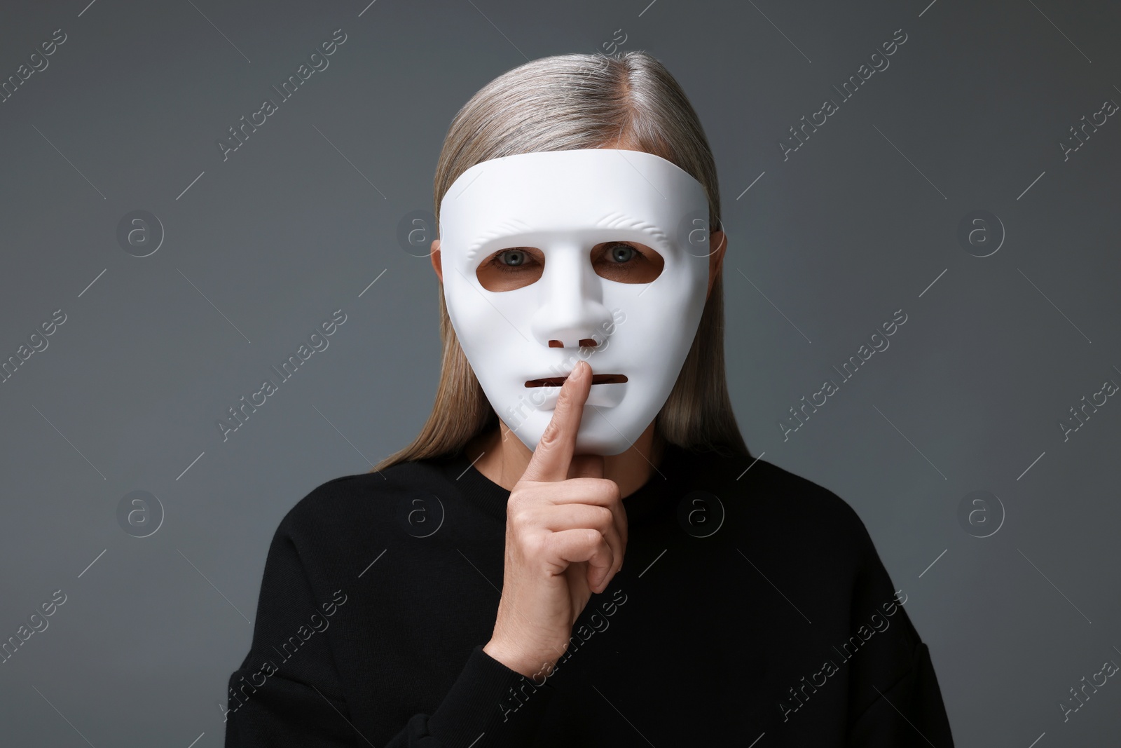 Photo of Multiple personality concept. Woman in mask showing hush gesture on gray background