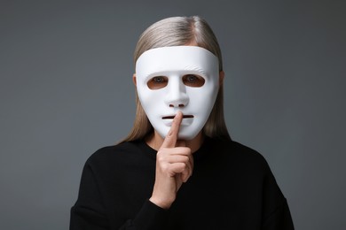 Photo of Multiple personality concept. Woman in mask showing hush gesture on gray background