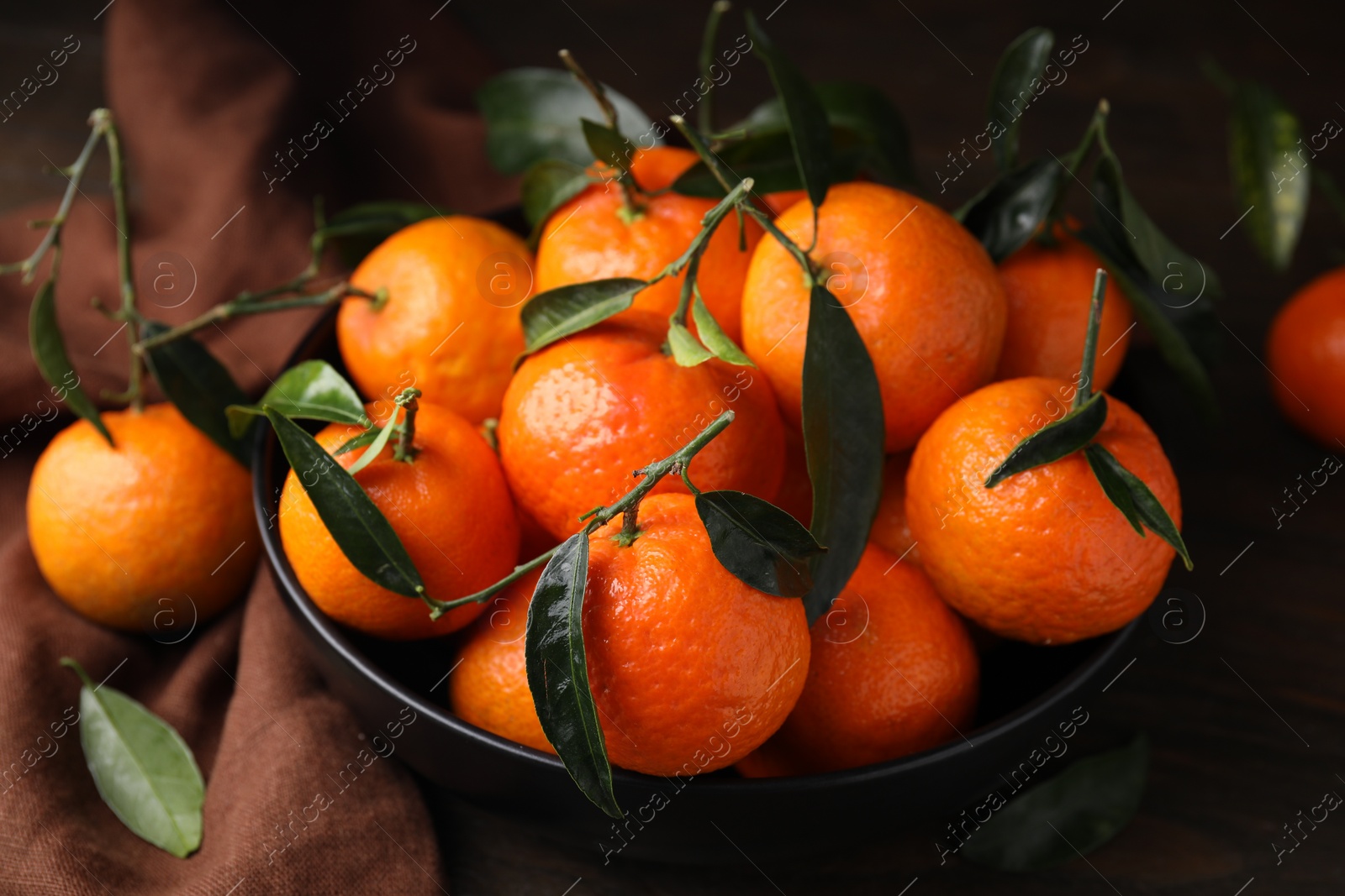 Photo of Fresh ripe tangerines with green leaves in bowl on table, closeup