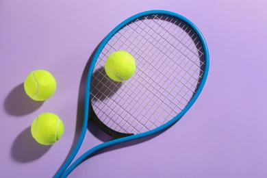 Tennis racket and balls on violet background, flat lay. Sports equipment