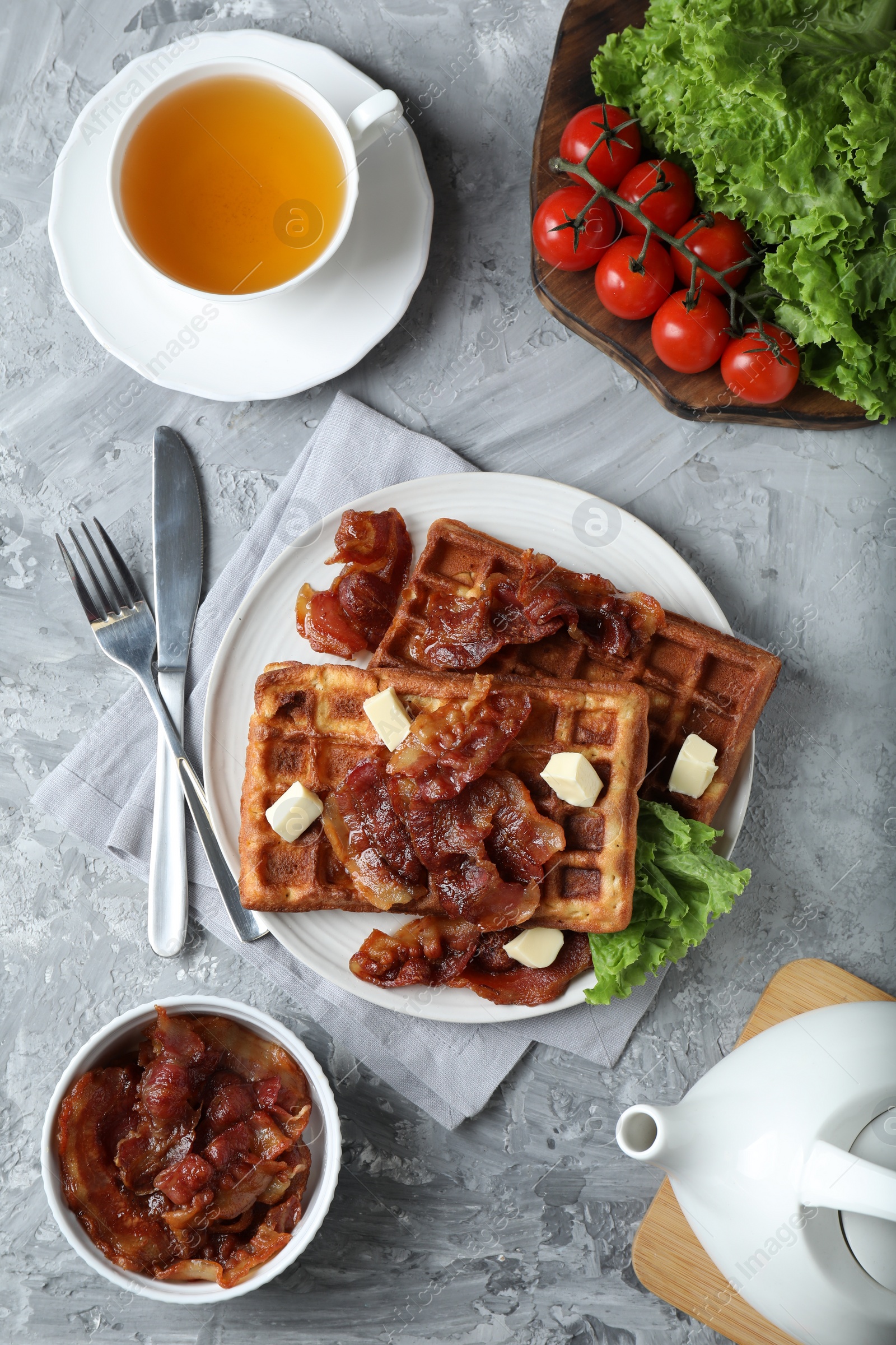 Photo of Delicious Belgium waffles served with fried bacon and butter on grey table, flat lay