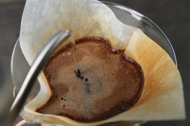 Photo of Pouring hot water into glass chemex coffeemaker with paper filter and coffee, closeup