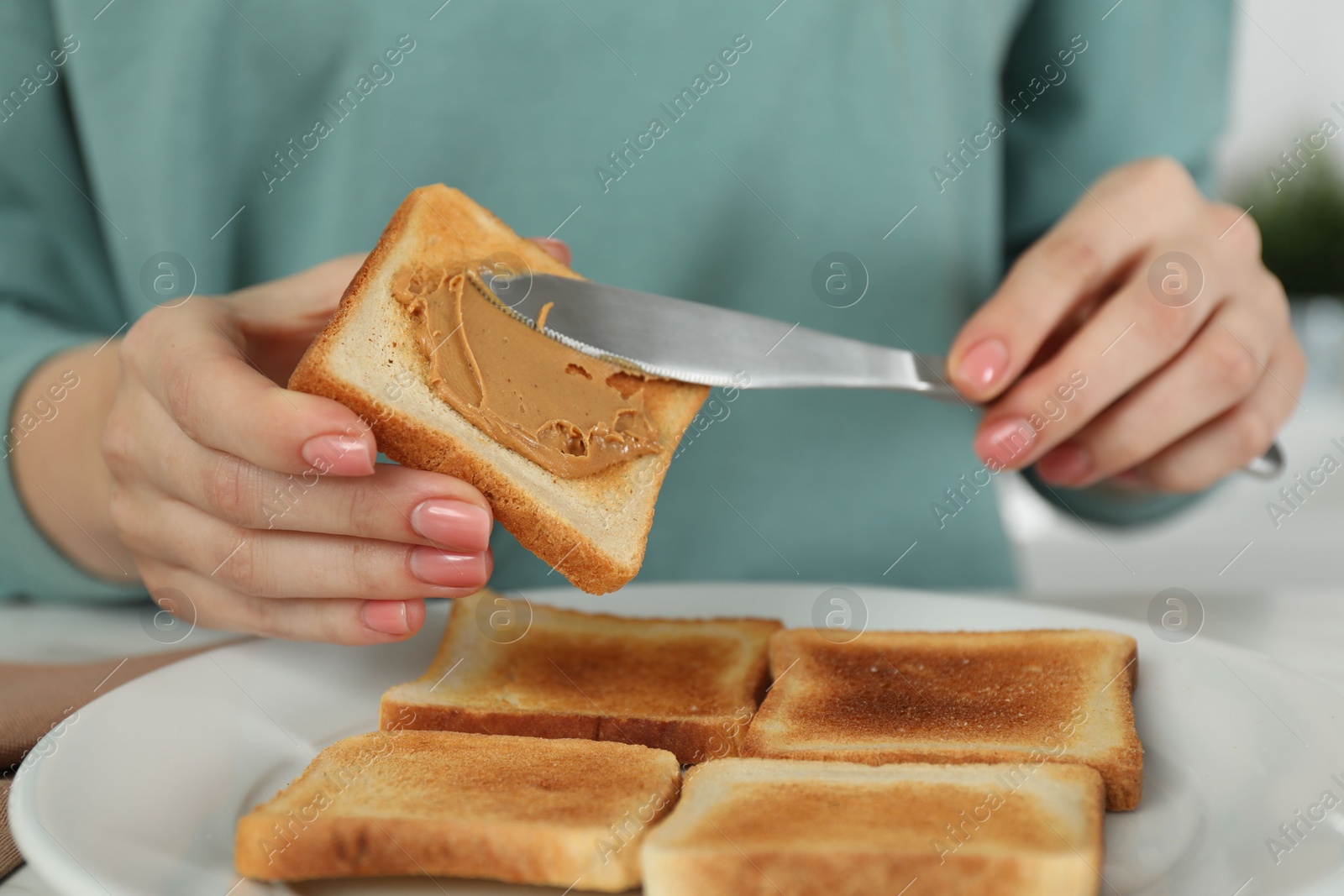 Photo of Woman spreading tasty nut butter onto toast at table, closeup