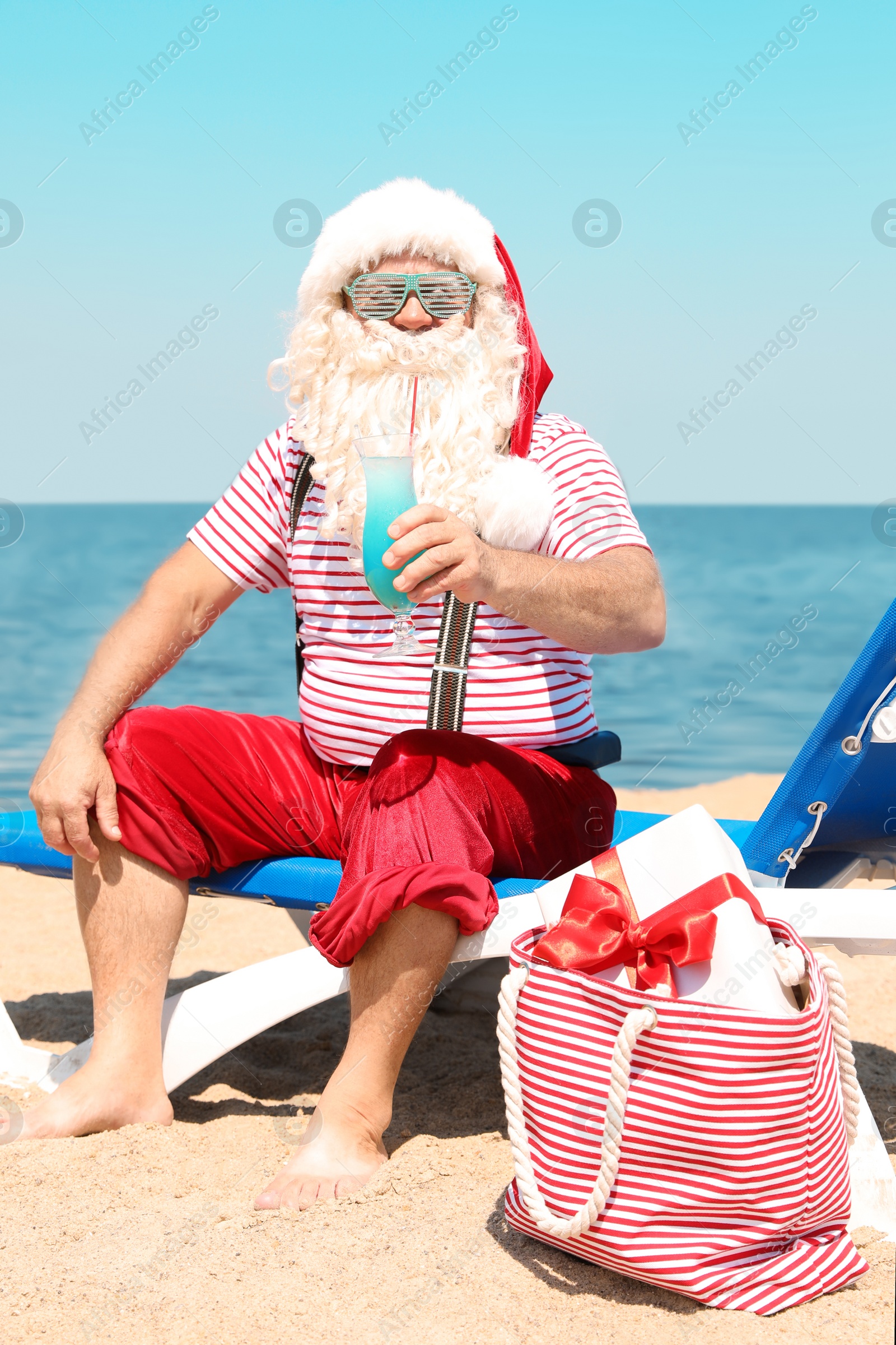 Photo of Authentic Santa Claus with cocktail resting on lounge chair at resort