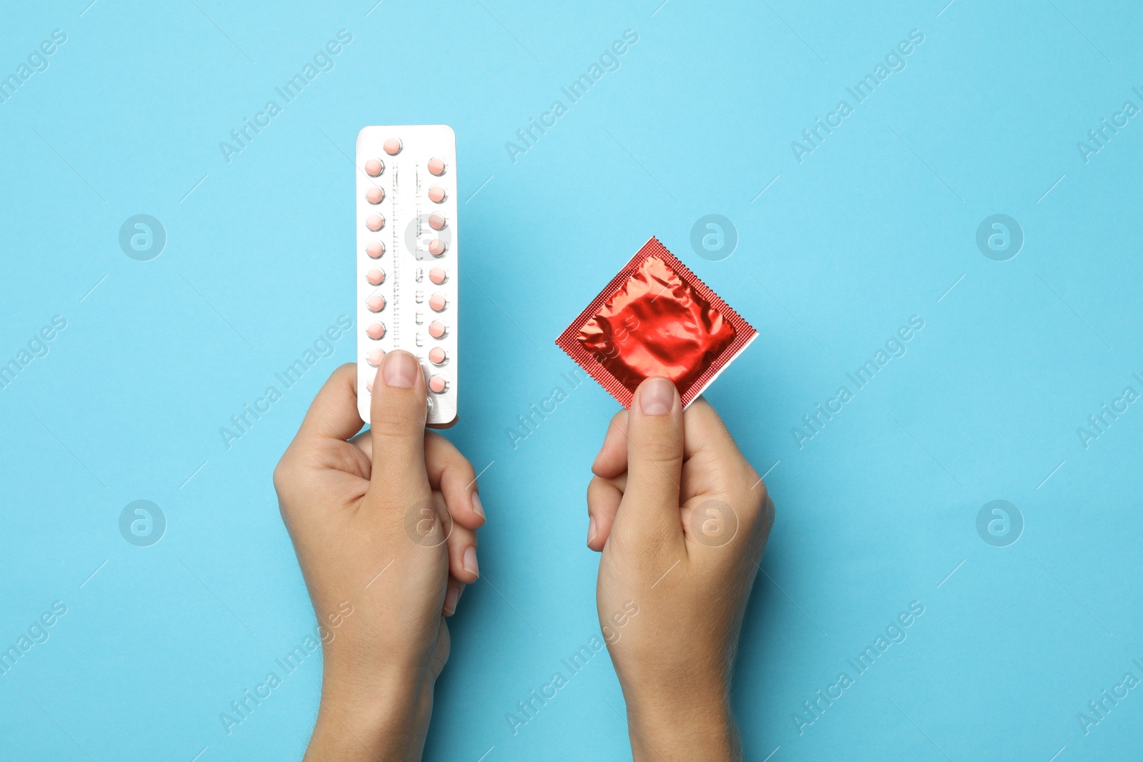 Photo of Woman holding condom and birth control pills on blue background, top view. Safe sex