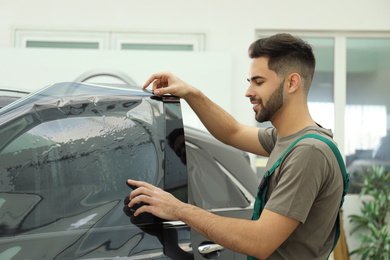 Photo of Worker tinting car window with foil in workshop